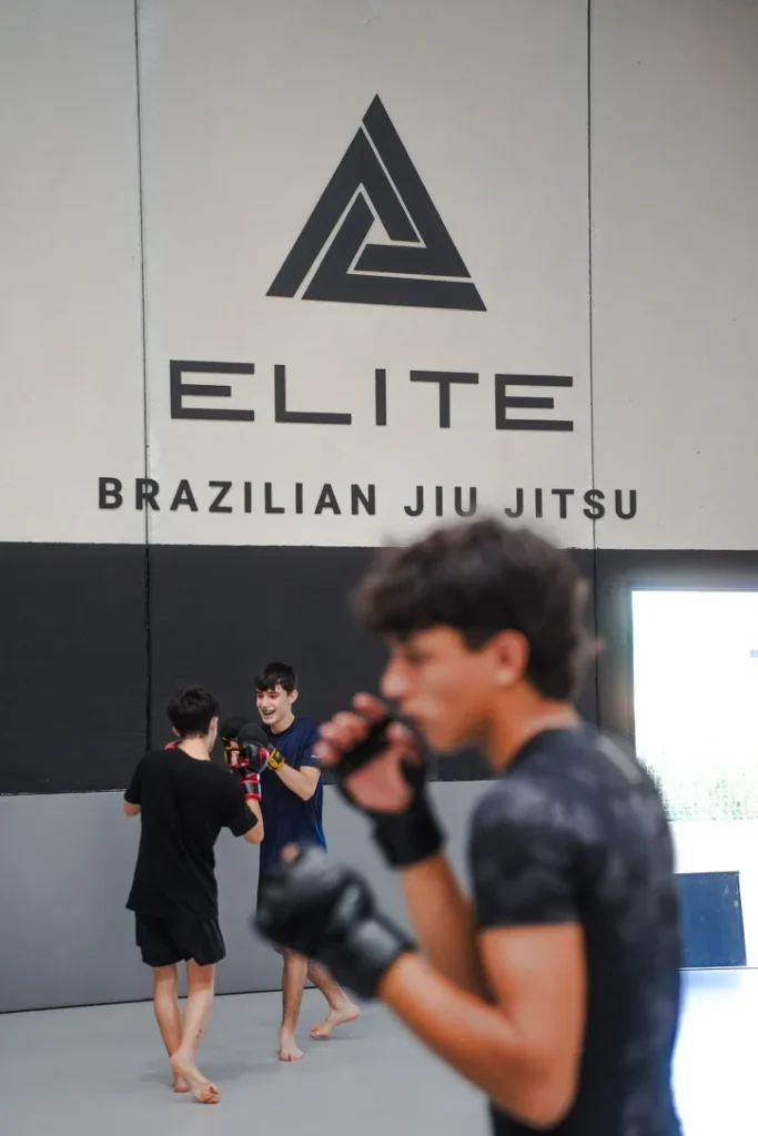 Alumnos de la clase de MMA de Elite BJJ trabajando golpeo por parejas bajo el logo de la escuela