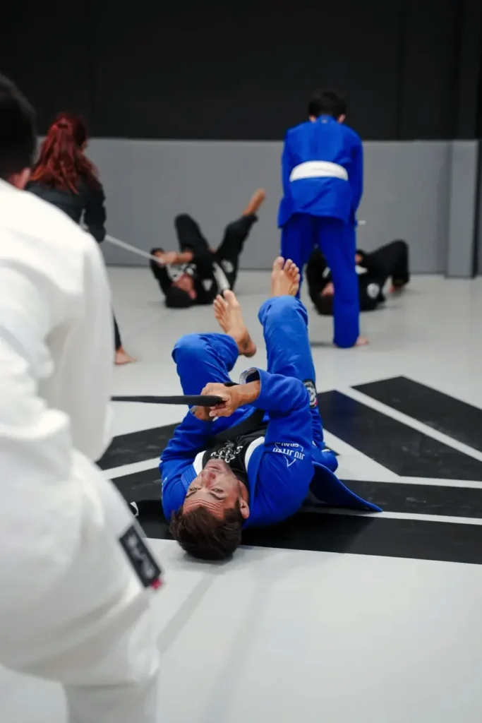 Alumno de Elite BJJ con kimono azul entrenando en el suelo durante la clase de BJJ